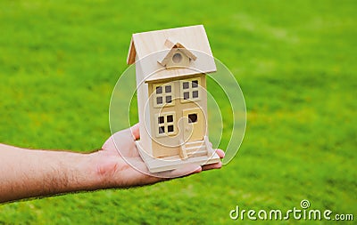 House in caring female hands. Man holding wooden model house in hands on grass background. Stock Photo