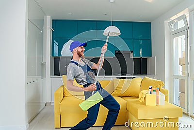 Funny picture of male cleaning worker in special clothes playing with a mop as a guitar in the kitchen Stock Photo