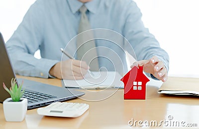 A House on desk envelope with man signing purchase documents in background. while hand complete the insurance policy, rental Stock Photo