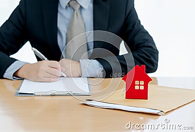 A House on document envelope with man signing purchase documents in background. while hand complete the insurance policy, rental Stock Photo