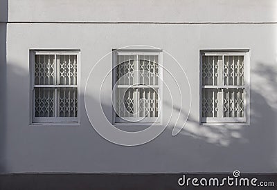 House exterior with triple wooden casement windows on white wall and white steel folding gates inside Stock Photo