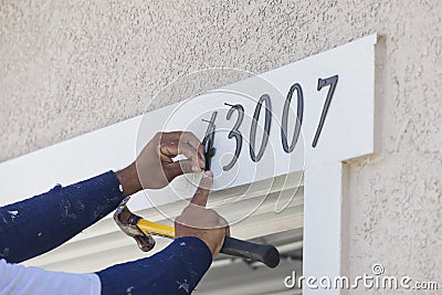 House Painter Contractor Nails Address Numbers to House Facade Stock Photo