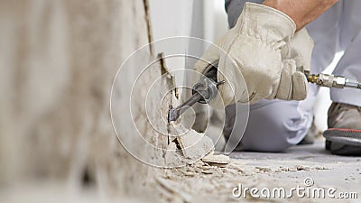 House renovation concept, construction worker breaks the old plaster of the wall with pneumatic air hammer chisel, close up with Stock Photo