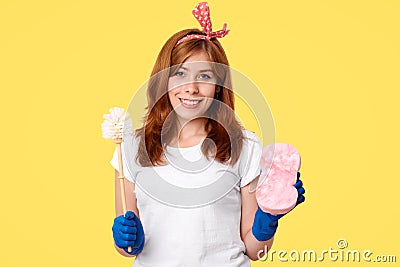 Housecleaning concept. Cheerful positive young female does spring cleaning at house, holds brush and sponge, wears casual outfit a Stock Photo