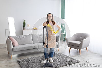 Housecleaning service. Happy young maid with vacuum cleaner standing in middle of tidy living room, full length portrait Stock Photo