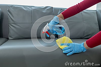 The housekeeper is cleaning the living room inside the house, Cleaning the couch with a towel and sanitizer, Wear rubber gloves Stock Photo
