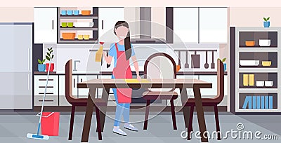 Housewife in apron wiping dinning table by dust cloth girl doing housework cleaning service housekeeping concept full Vector Illustration