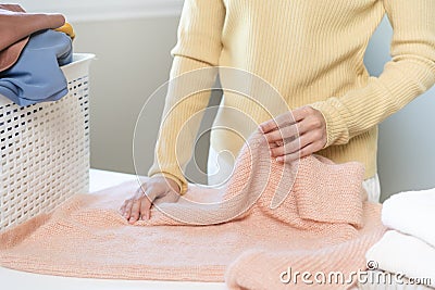 Housewife, asian young woman hand in many folding freshly shirts, sweaters or dress on desk, table after washing clean clothes and Stock Photo