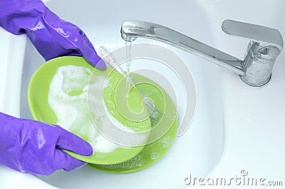 Housewife.Wash green plates under running water. Hands in protective rubber gloves Stock Photo