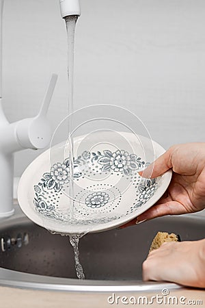 housewife washes a plate in the kitchen under running water Stock Photo