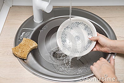 housewife washes a plate in the kitchen under running water Stock Photo