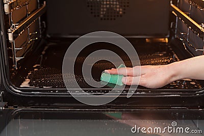 Housework and housekeeping concept. Scrubbing the stove and oven. Close up of female hand with green sponge cleaning the kitchen o Stock Photo