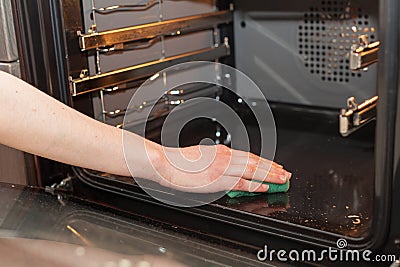 Housework and housekeeping concept. Scrubbing the stove and oven. Female hand with green sponge cleaning the kitchen oven.. Stock Photo