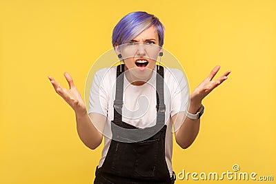 How could you? Portrait of outraged hipster woman standing in bewilderment with raised hands. yellow background, studio shot Stock Photo