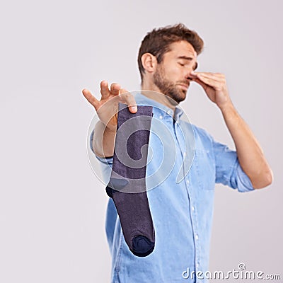 How old is this sock. Studio shot of a handsome young man holding an unpleasant smelling sock against a gray background. Stock Photo