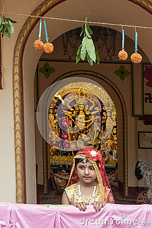 Howrah,India -October 26th,2020 : Bengali girl child posing with Goddess Durga in background, inside old age decorated home. Durga Editorial Stock Photo