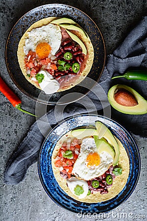 Huevos Rancheros Tostadas, Mexican breakfast consisting of toasted tortilla, chopped tomato and onion, jalapeno and beans, topped Stock Photo