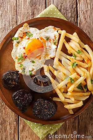 Huevos rotos con morcilla fried egg with fries and blood sausage close-up in a plate. vertical top view Stock Photo