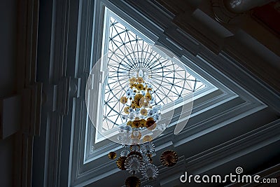 Huge chandelier is hanging down from ceileng through triangle hole. Stock Photo
