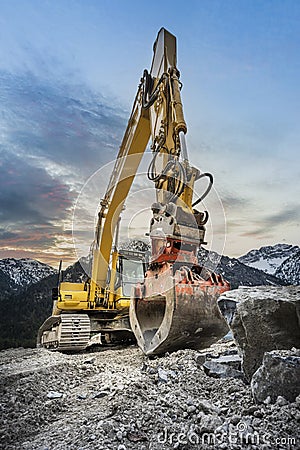 huge clamshell grab excavator for natural stone masonry in front of alp mountains Stock Photo