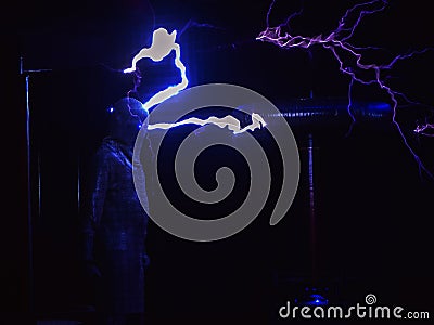 Huge electric coils spew lightning striking a man dressed in a chain suit. Electric show Stock Photo