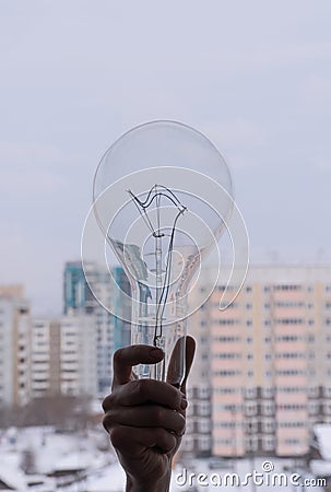 huge electric light bulb in hand. incandescent lamp on the background of residential buildings. Stock Photo