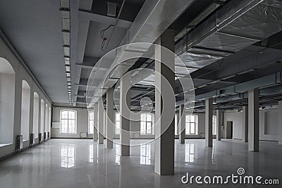 Huge empty open space in the old factory building with rows of columns, large windows and pipes under the ceiling Stock Photo