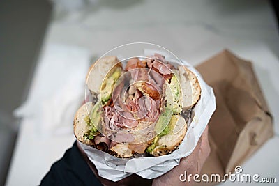 huge everything bagel stuffed with ingredients like ham cheese bacon and avocado for breakfast Stock Photo