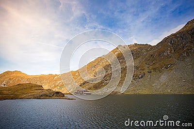 Huge lake in the mountains with a little house on the dock. Nice blue sky with some clouds. Shot in Romania, Transfagarasan Stock Photo