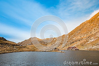 Huge lake in the mountains with a little house on the dock. Nice blue sky with some clouds. Shot in Romania, Transfagarasan Stock Photo