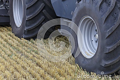 The wide wheels of the combine roll over the stubble of the harvested field Stock Photo