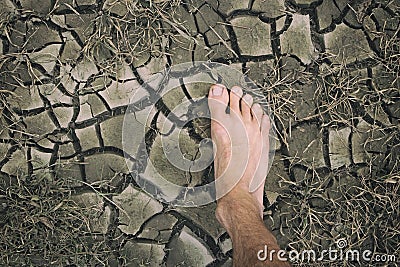 Human foot on dried cracked lifeless earth. Man`s barefoot on dry soil with dead plants. Barren land because of ecological Stock Photo