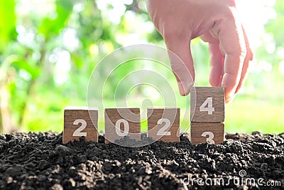 Human hand change year 2023 to 2024 in wooden blocks with growing plant at sunrise. Welcome new year 2024 Stock Photo