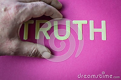 Human hand hiding the word Truth written with plastic letters on a bright pink paper background Stock Photo