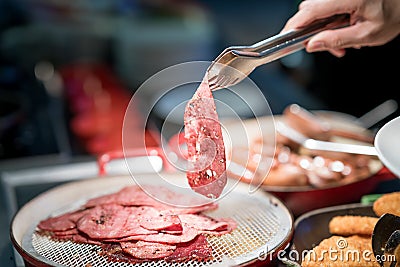 Human hand holding tongs over plate of sliced smoked meat in bar Stock Photo
