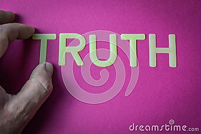 Human hand holding the word Truth written with plastic letters on a bright pink paper background Stock Photo