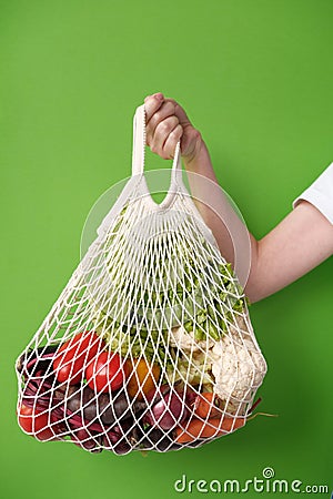 Human hand holds string bag mesh with vegetables and fruits. Zero waste shopping concept. Stock Photo