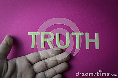 Human hand showing the word Truth written with plastic letters on a bright pink paper background Stock Photo