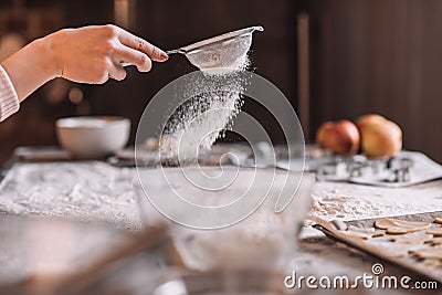Human hand sifting flour above kitchen table Stock Photo