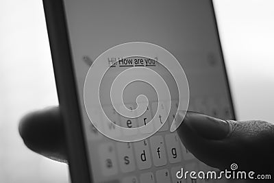 Human hand typing on a white smartphone a message Hi, how are you. BW photo Stock Photo