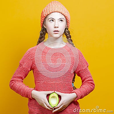 Human Health Concepts. One Teenage Girl In Coral Knitted Clothing With Split Avocado Fruit In Front of Belly as a Demonstration of Stock Photo