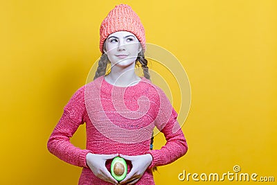 Human Health Concepts. Teenager Girl In Coral Knitted Clothing With Split Avocado Fruit In Front of Belly as a Demonstration of Stock Photo