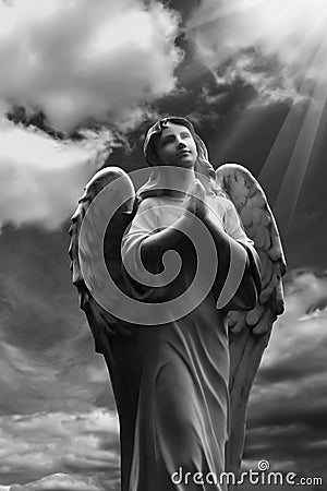 Human soul as angel with wings looking up at the sky in rays of light. Ancient statue. Black and white image Stock Photo