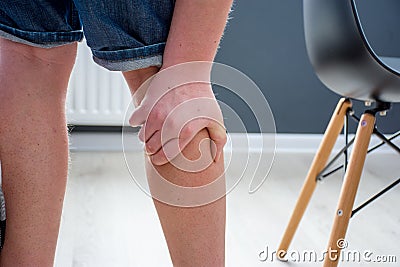 Human, who had been elevated from chair, holding his palm over calf or gastrocnemius muscle, which grabbed cramp with severe pain. Stock Photo