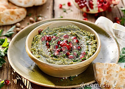 Hummus. Herb hummus with the addition of pomegranate seeds, parsley, olive oil and aromatic spices in a ceramic pot on a wooden Stock Photo