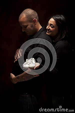 Humorous Mixed Race Couple Holding New White Baby Shoes on Black Stock Photo