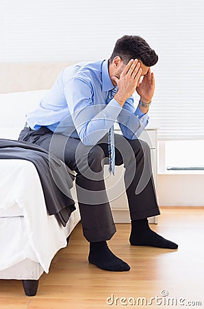 Hungover businessman sitting at edge of bed Stock Photo
