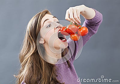 Hungry beautiful girl eating up tomatoes with appetite and greed Stock Photo