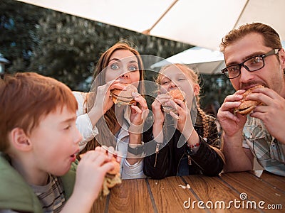 Hungry family eating hamburgers, sitting at a table in a fast food restaurant Stock Photo