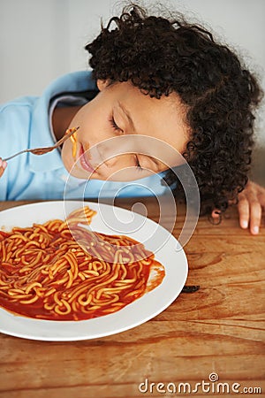 Hungry, food and child eating spaghetti by the wooden kitchen counter for lunch at home. Pasta, tomato and boy kid Stock Photo